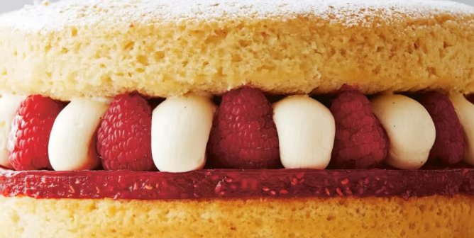 A tiered sponge cake with frosting and raspberries
