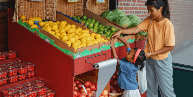 A mother and daughter shopping for fruit in a market